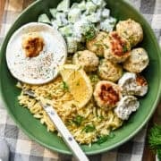 Close up view of feta chicken meatballs in a green bowl with orzo, cucumbers and a dill yogurt sauce.