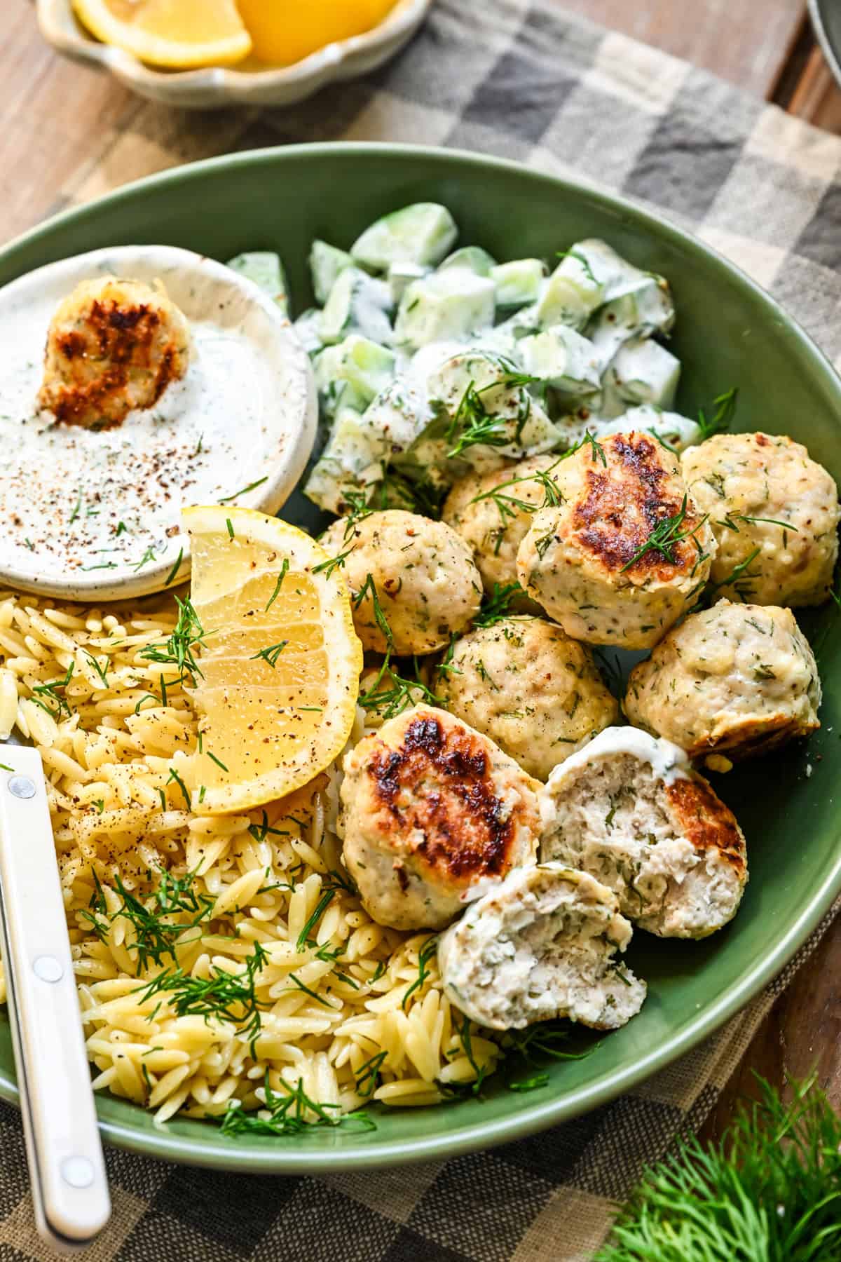 Close up view of feta chicken meatballs in a green bowl with orzo, cucumbers and a dill yogurt sauce.
