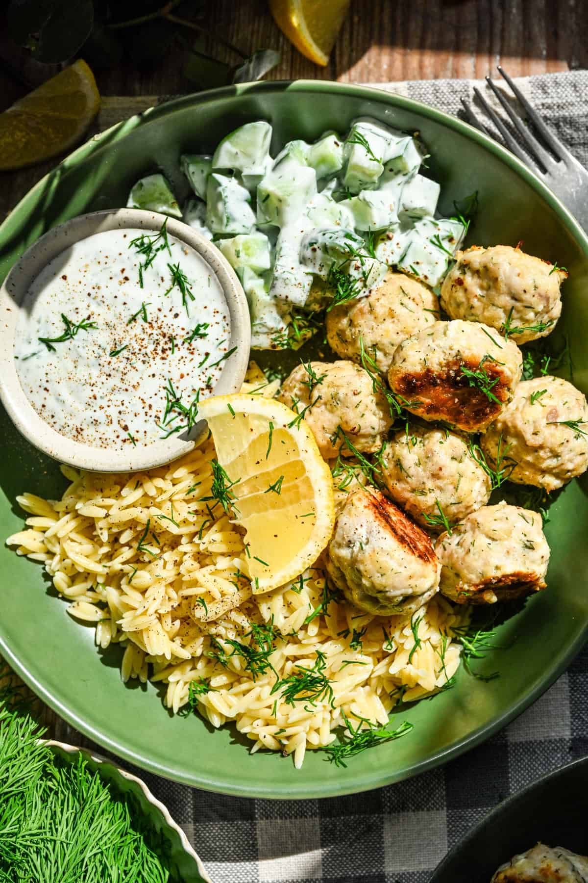 Close up view of feta chicken meatballs in a green bowl with orzo, cucumbers and a dill yogurt sauce.