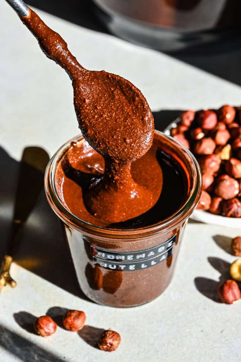 Front view of nutella dripping of a spoon into a small glass jar.