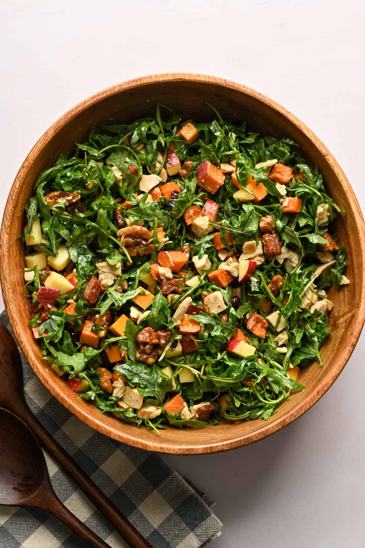 Overhead view of bacon apple cheddar arugula salad tossed together in a wood salad bowl.
