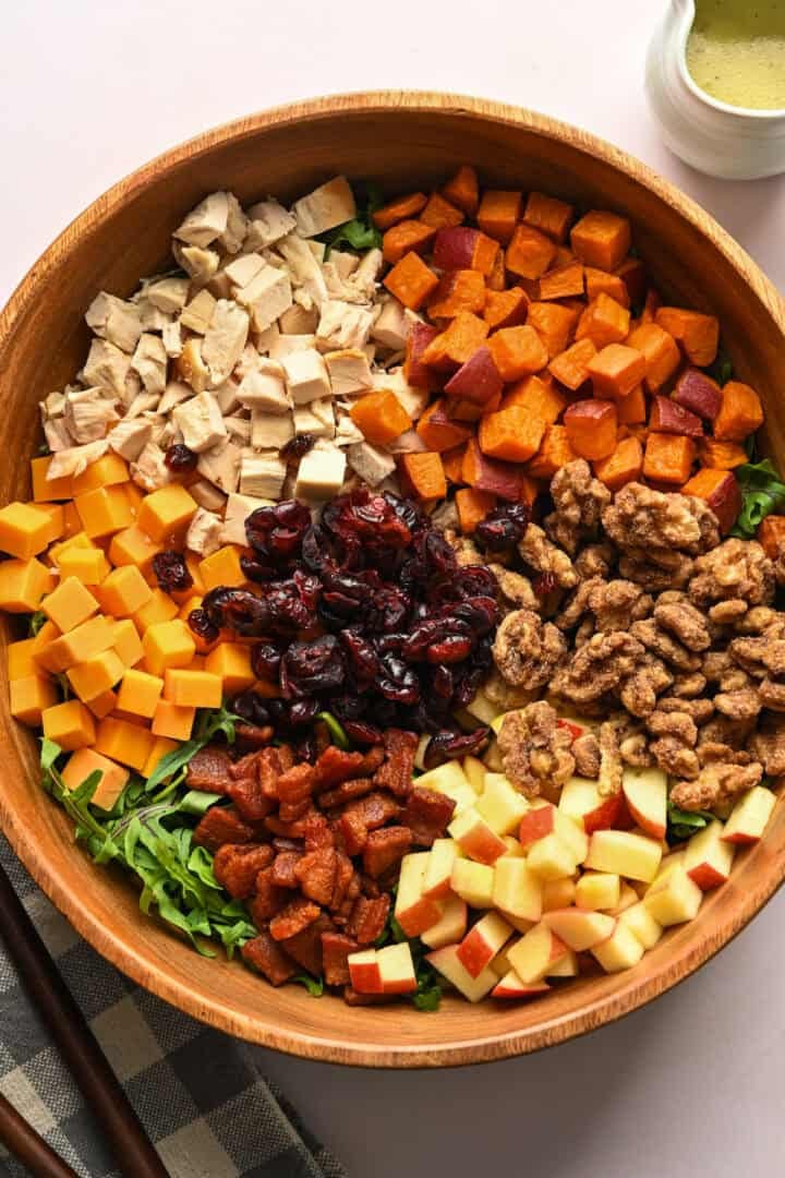 Overhead view of bacon apple cheddar arugula salad before tossing all of the ingredients together in a wood salad bowl.