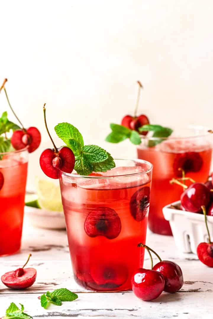Side view of tart cherry old fashioned cocktail with fresh cherries and mint garnish.