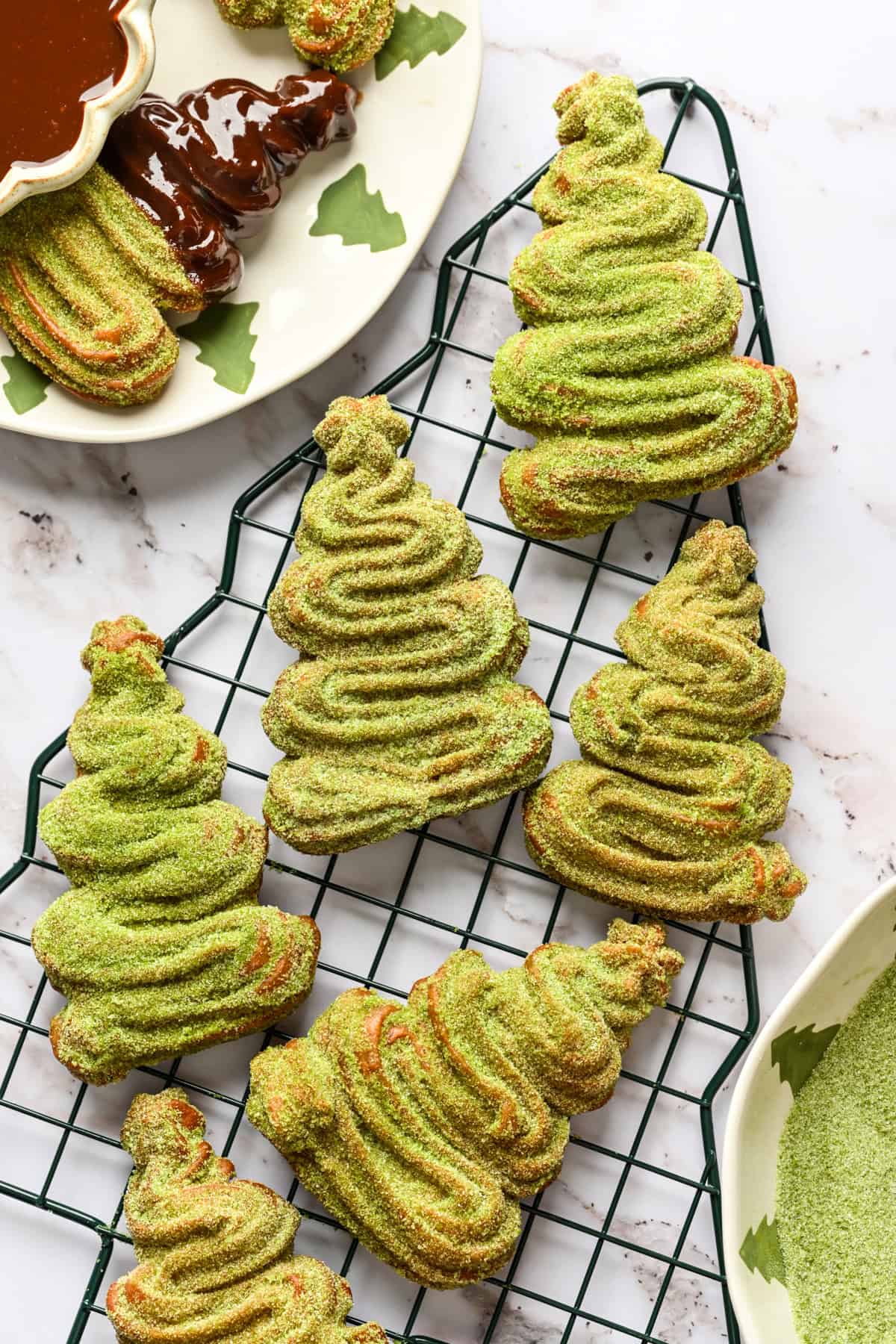 Close up overhead view of christmas tree shaped churros coated in matcha sugar on a christmas tree cooling rack.