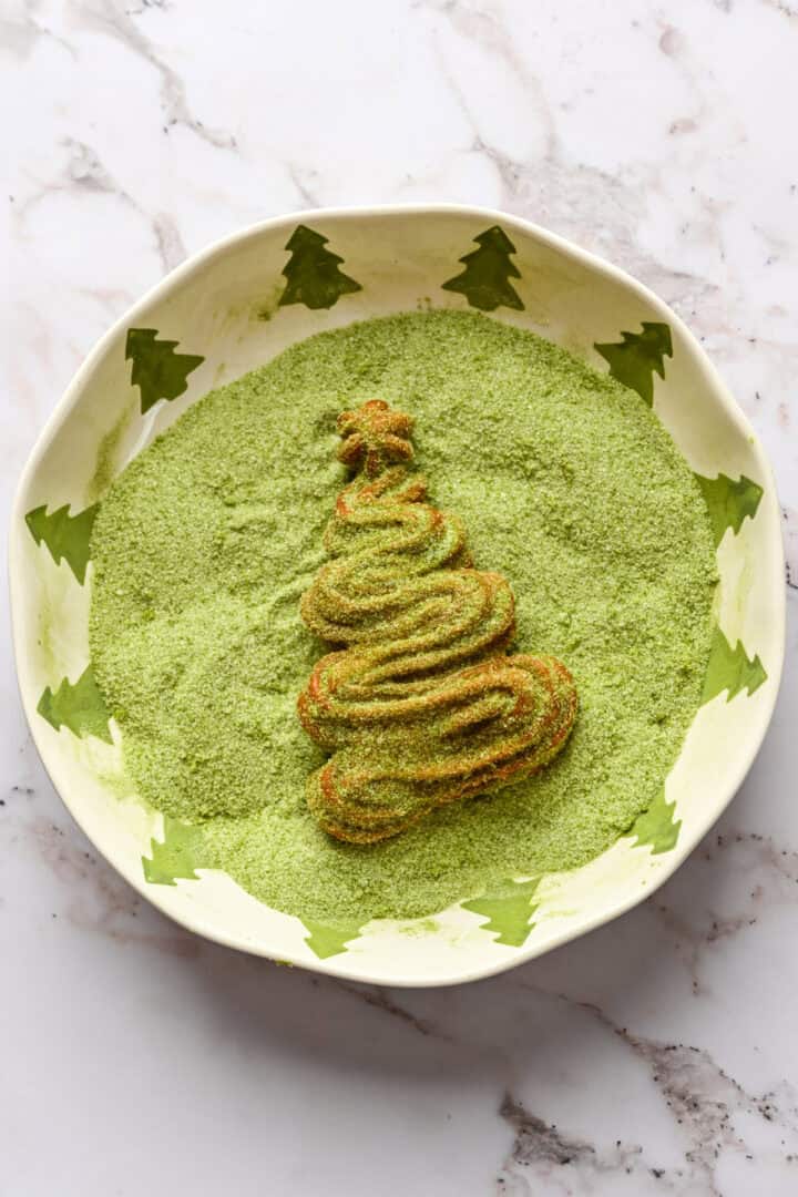 Christmas tree churro in a bowl of matcha sugar.