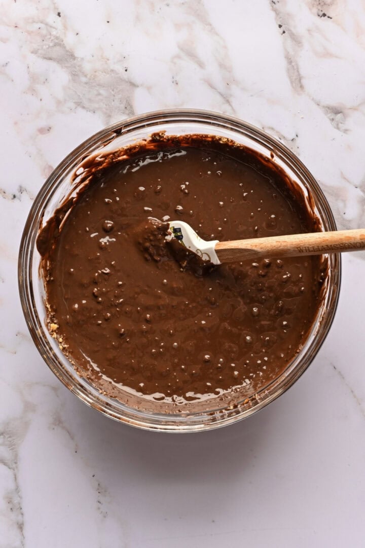 Melted chocolate and chopped hazelnuts in a bowl after stirring together.