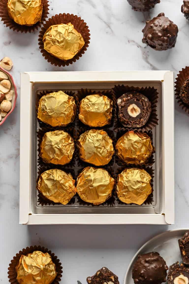 Overhead view of homemade ferrero rocher truffles wrapped in gold foil in a gift box with some unwrapped truffles around the box.
