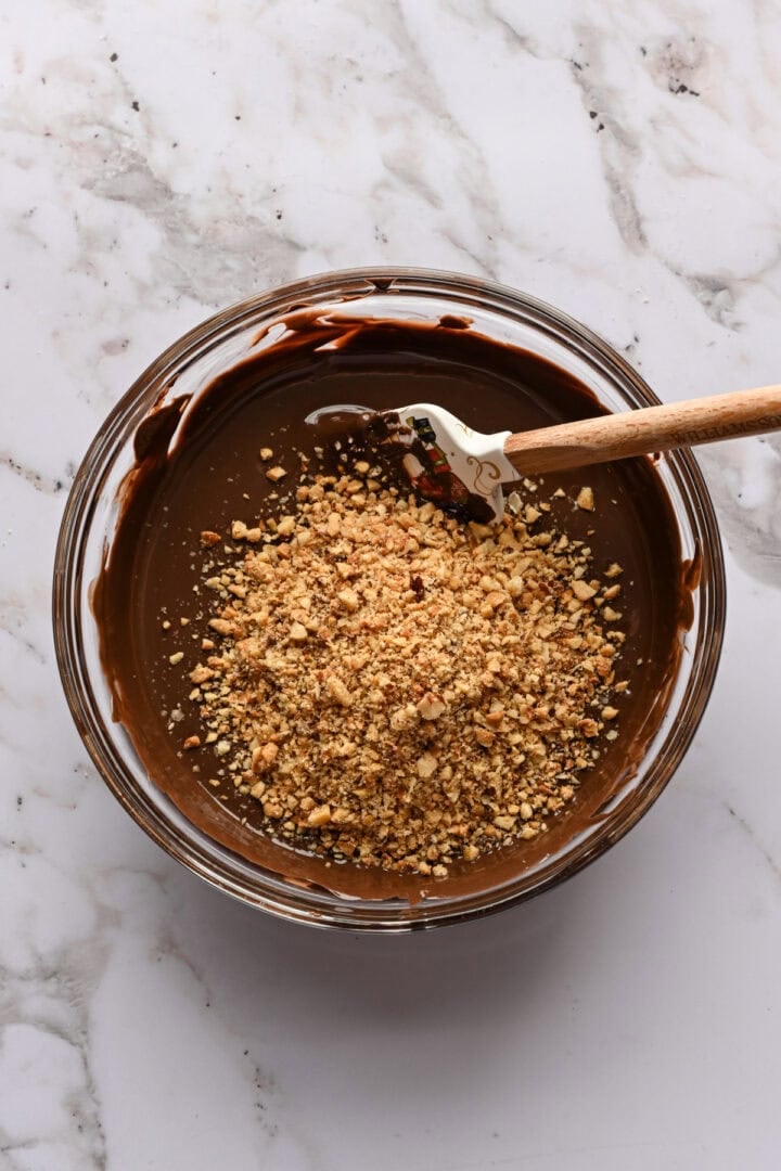 Melted chocolate and chopped hazelnuts in a bowl before stirring together.