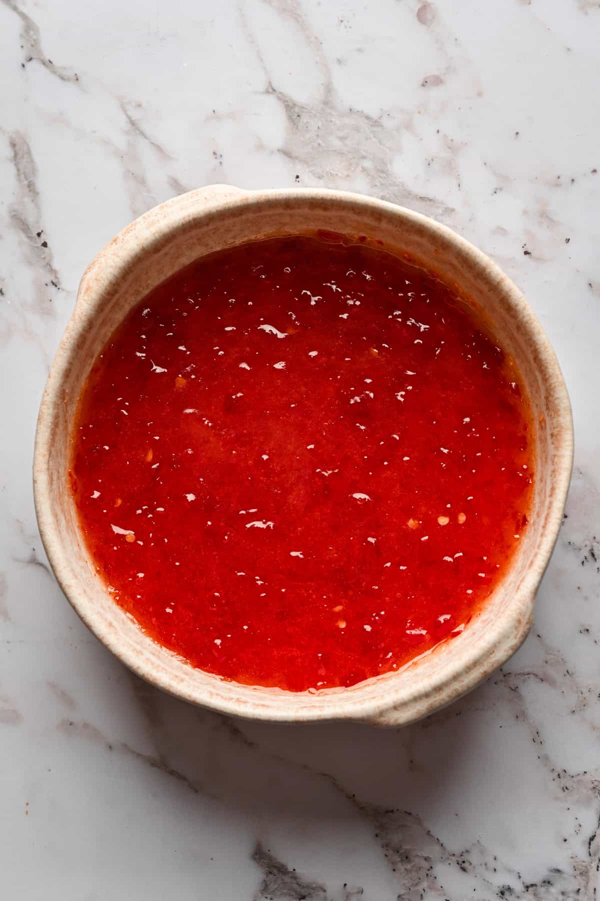 Overhead view of red pepper jelly in a pink bowl.