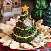 Christmas Tree Shaped Cheese Ball covered in herbs and decorated with pine nut garland and pomegranate ornaments.