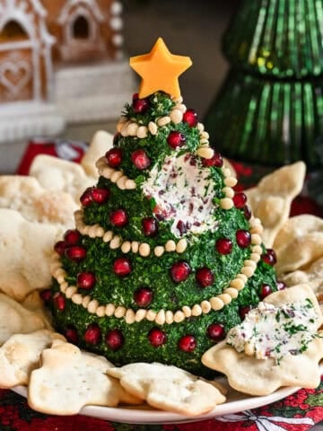 Christmas Tree Shaped Cheese Ball covered in herbs and decorated with pine nut garland and pomegranate ornaments.