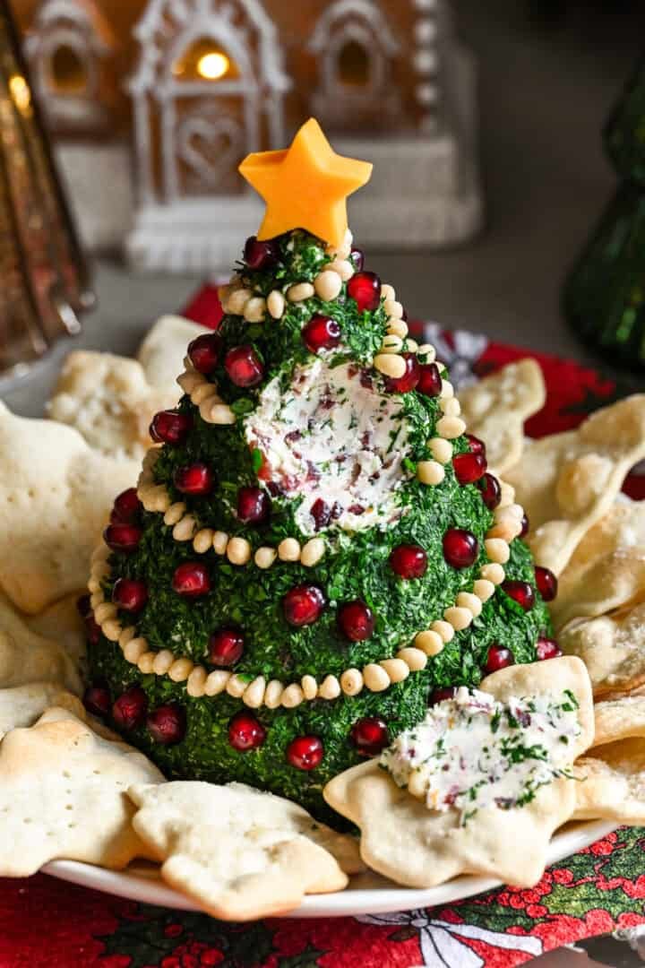 Christmas Tree Shaped Cheese Ball covered in herbs and decorated with pine nut garland and pomegranate ornaments.