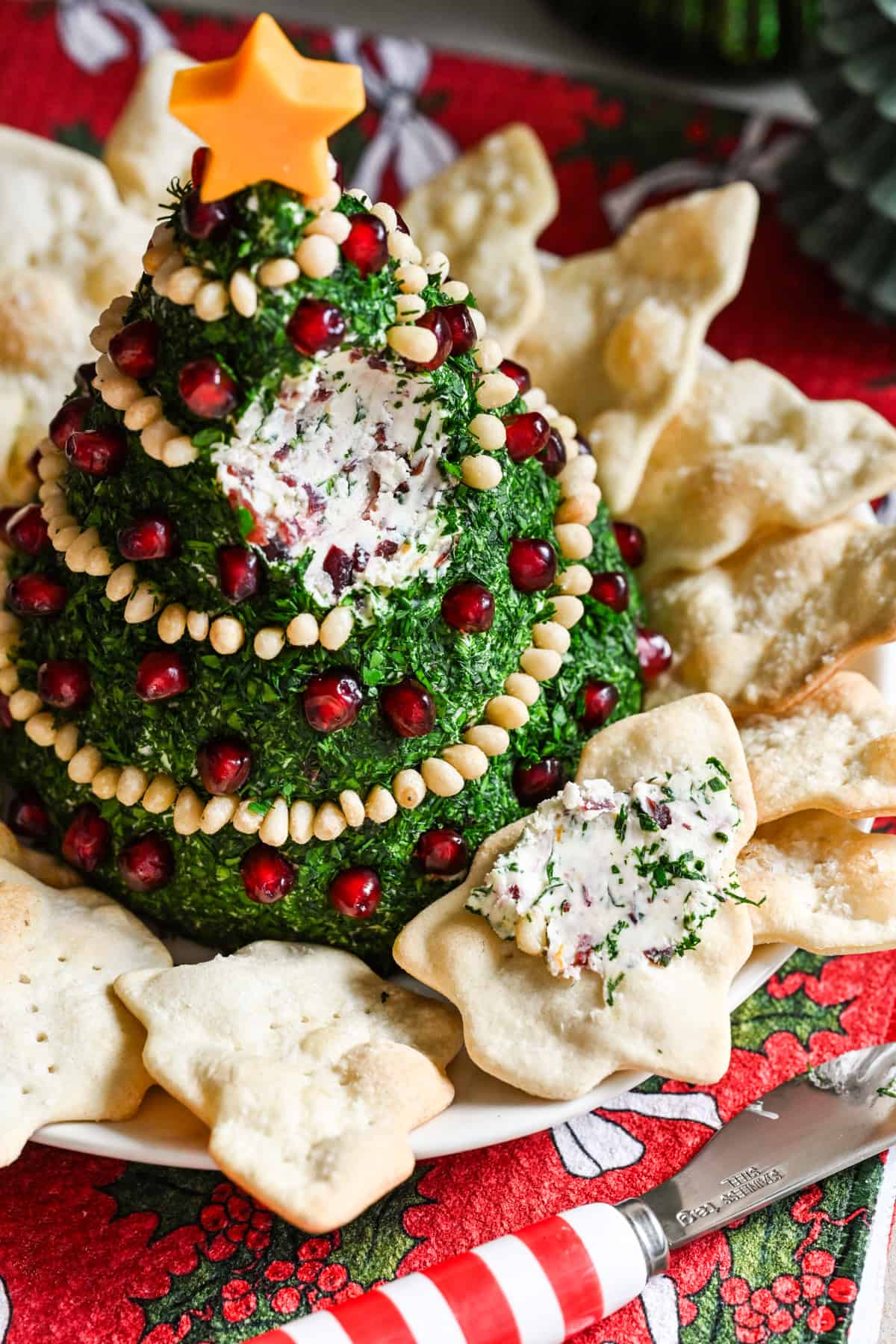 Christmas Tree Shaped Cheese Ball covered in herbs and decorated with pine nut garland and pomegranate ornaments.