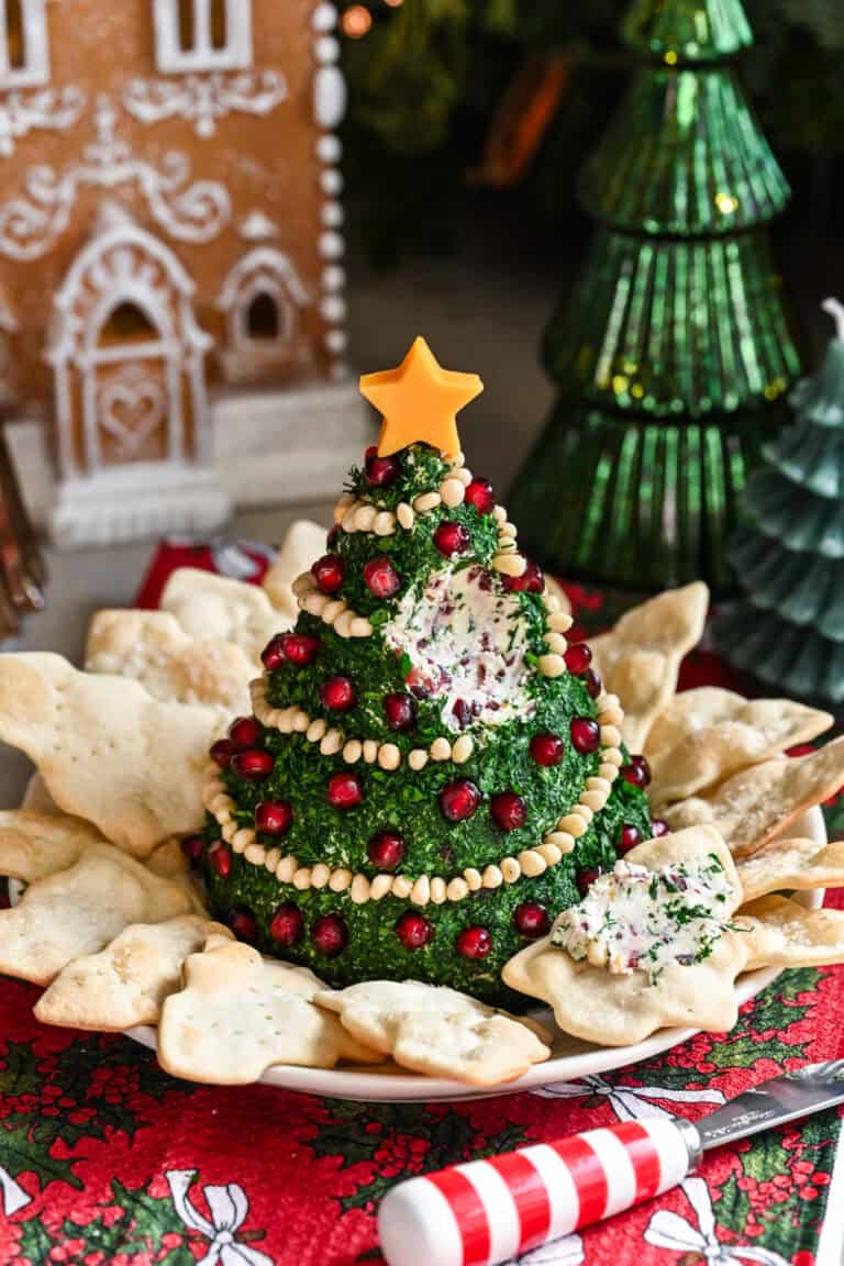 Christmas Tree Shaped Cheese Ball covered in herbs and decorated with pine nut garland and pomegranate ornaments.