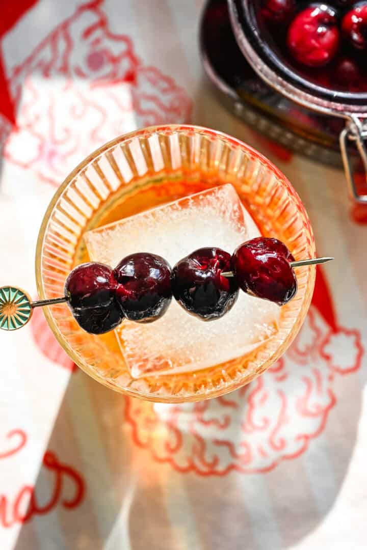 4 cocktail cherries on a cocktail pick atop a glass of bourbon.