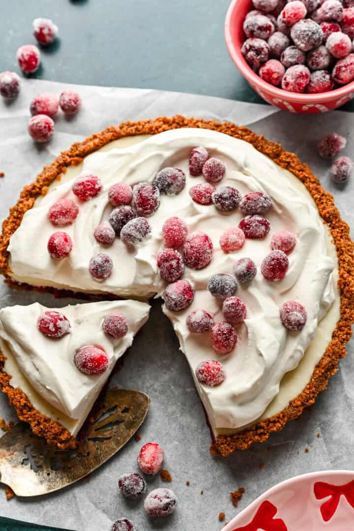 Cranberry white chocolate tart with whipped cream and sugared cranberries on top, with a slice cut out.