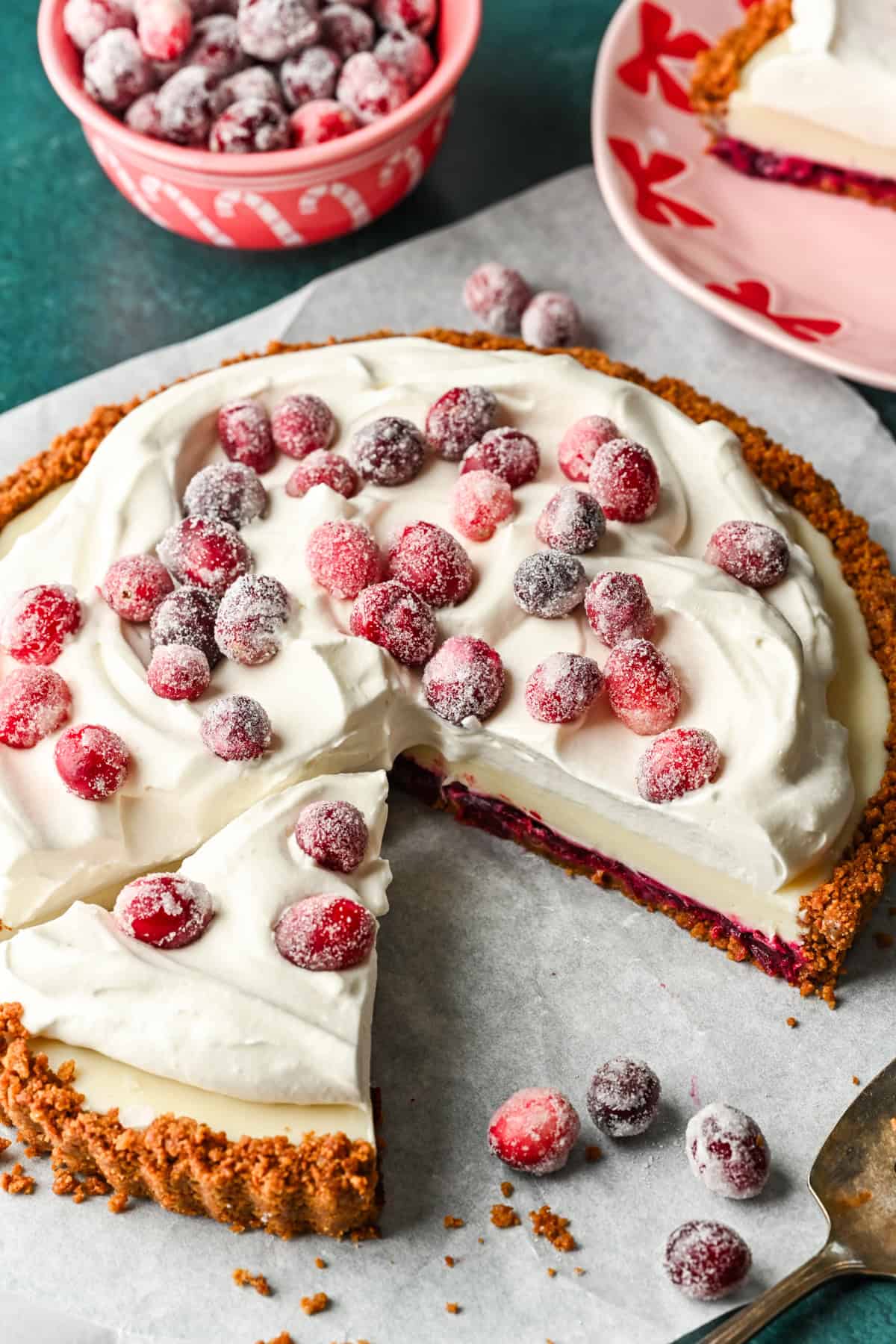 Canberry white chocolate tart with whipped cream and sugared cranberries on top, with a slice cut out.