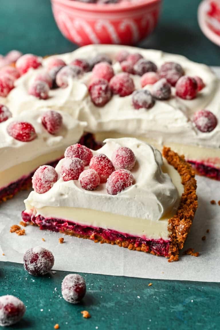 Close up side view of a slice of cranberry white chocolate tart with whipped cream and sugared cranberries on top.