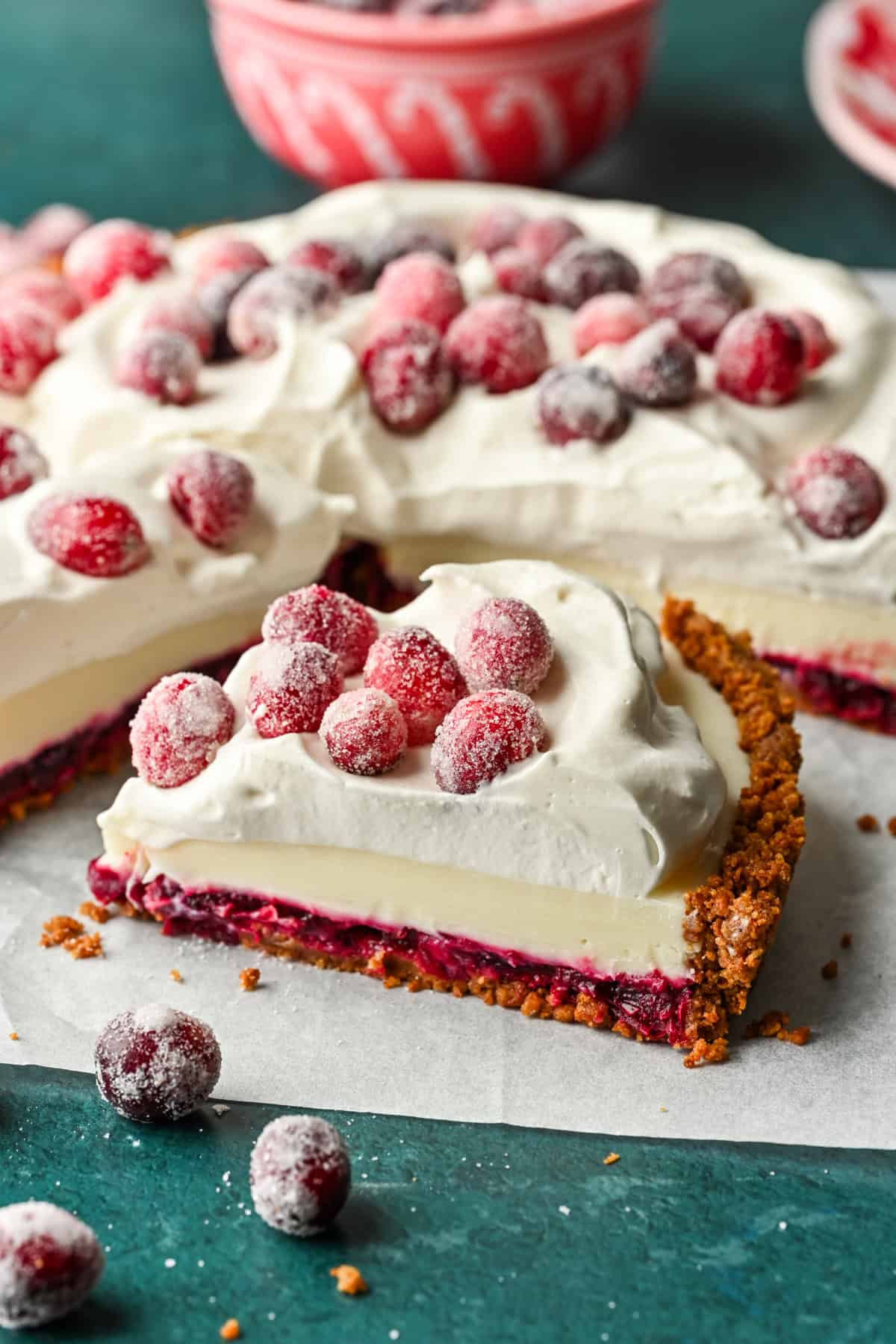 Close up side view of a slice of cranberry white chocolate tart with whipped cream and sugared cranberries on top.