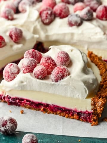 Close up side view of a slice of cranberry white chocolate tart with whipped cream and sugared cranberries on top.