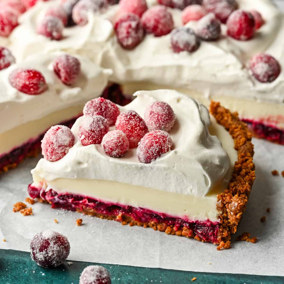 Close up side view of a slice of cranberry white chocolate tart with whipped cream and sugared cranberries on top.