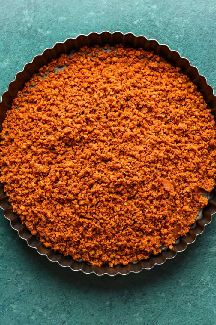 Gingersnap crust in a tart pan before pressing it in.
