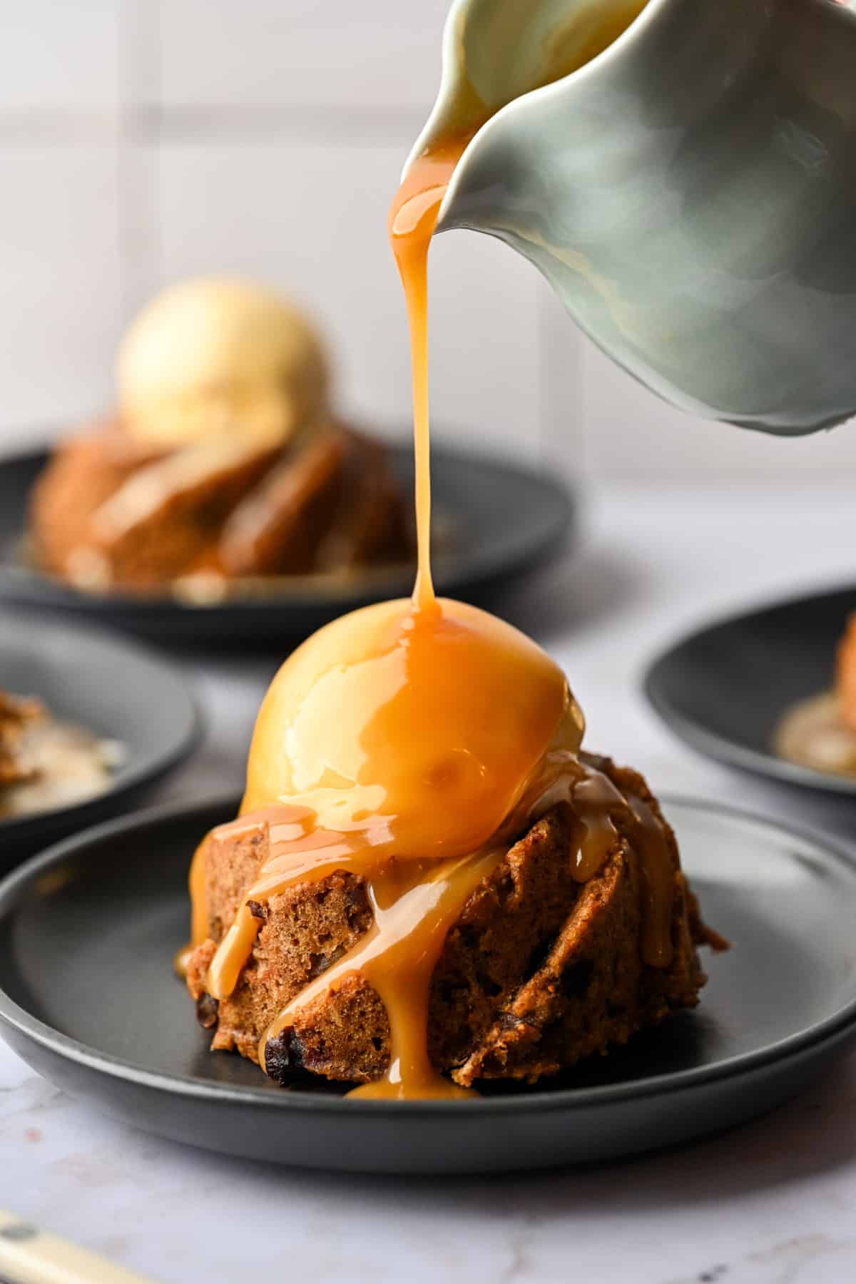 Pouring caramel sauce on top of ice cream atop a mini figgy pudding.