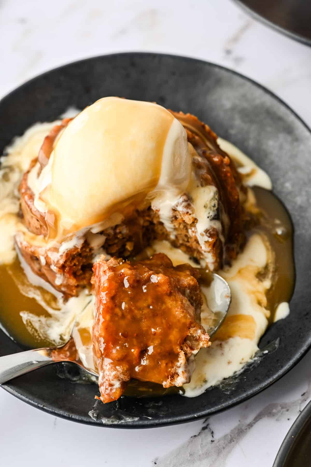 Close up view of figgy pudding with ice cream and caramel sauce with a bite taken out.