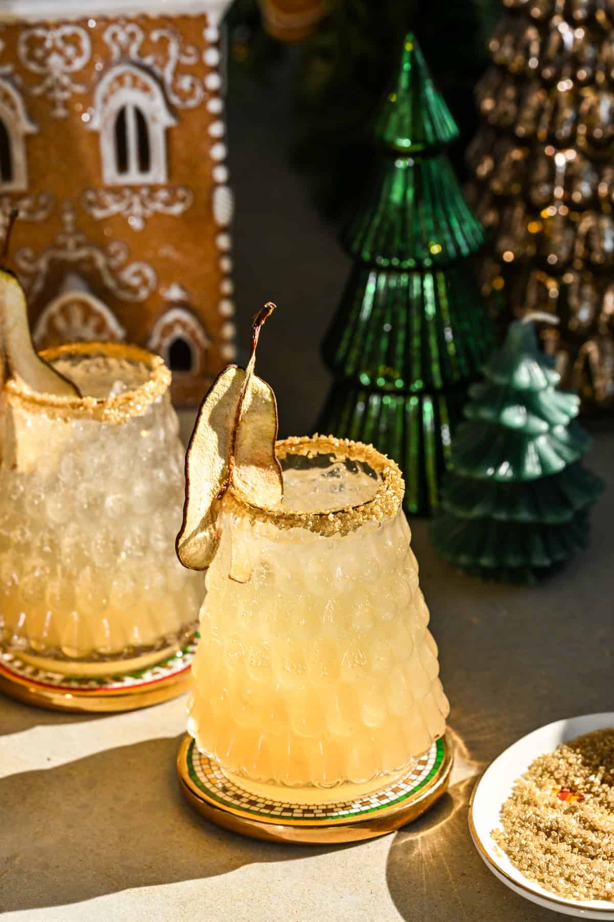 Side view of partridge in a pear tree cocktail in christmas tree glass with gold rim and dried pear garnish.