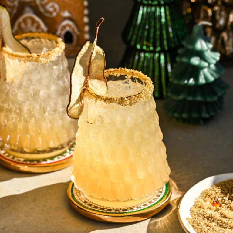 Side view of partridge in a pear tree cocktail in christmas tree glass with gold rim and dried pear garnish.