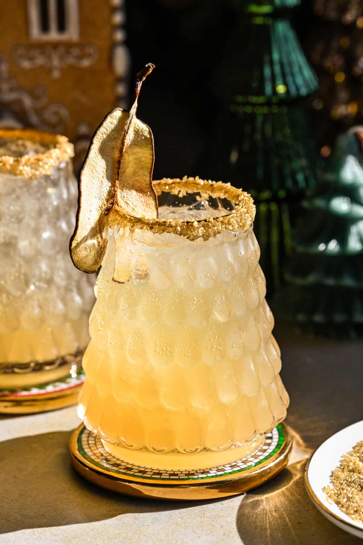 Side view of partridge in a pear tree cocktail in christmas tree glass with gold rim and dried pear garnish.