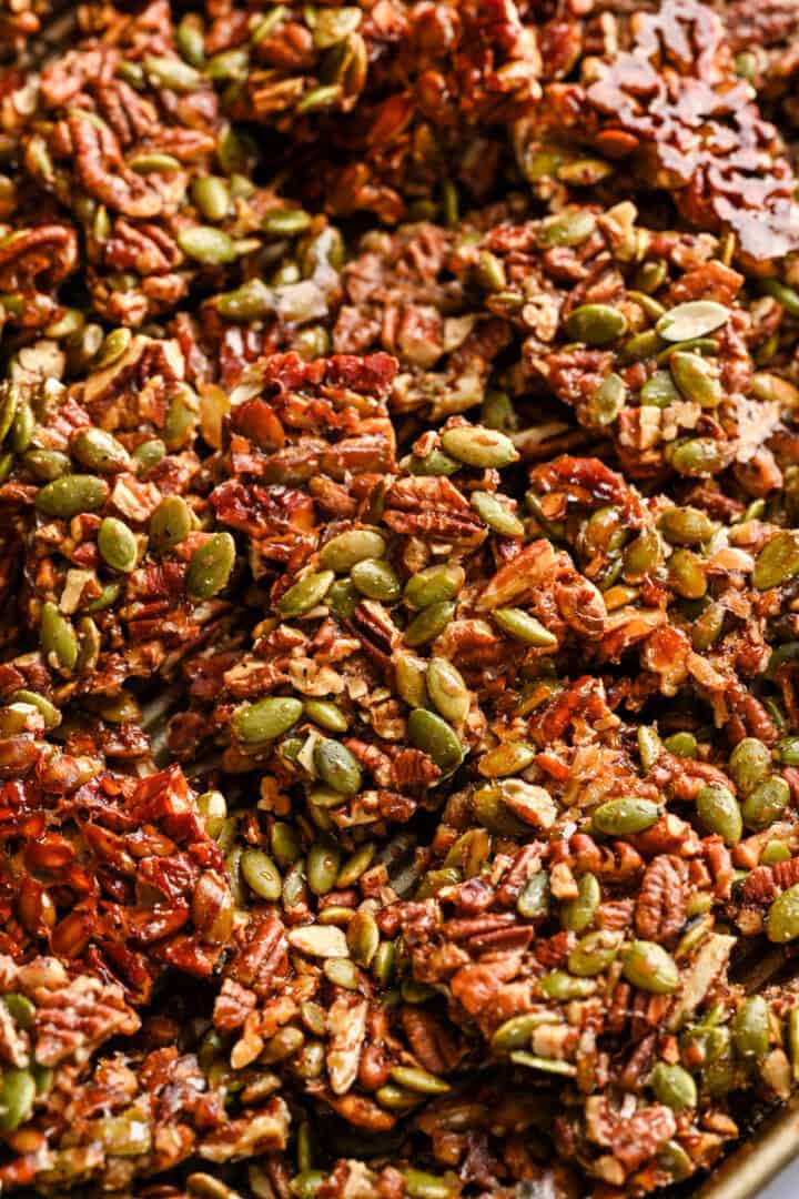 Pecan pepita brittle on baking sheet after baking, broken up into pieces.
