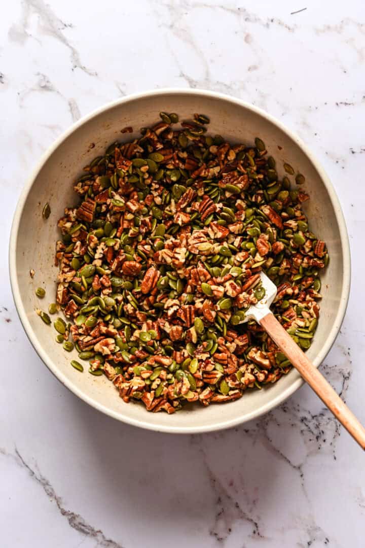 Pecans and pepitas mixed together in a bowl with maple syrup mixture.