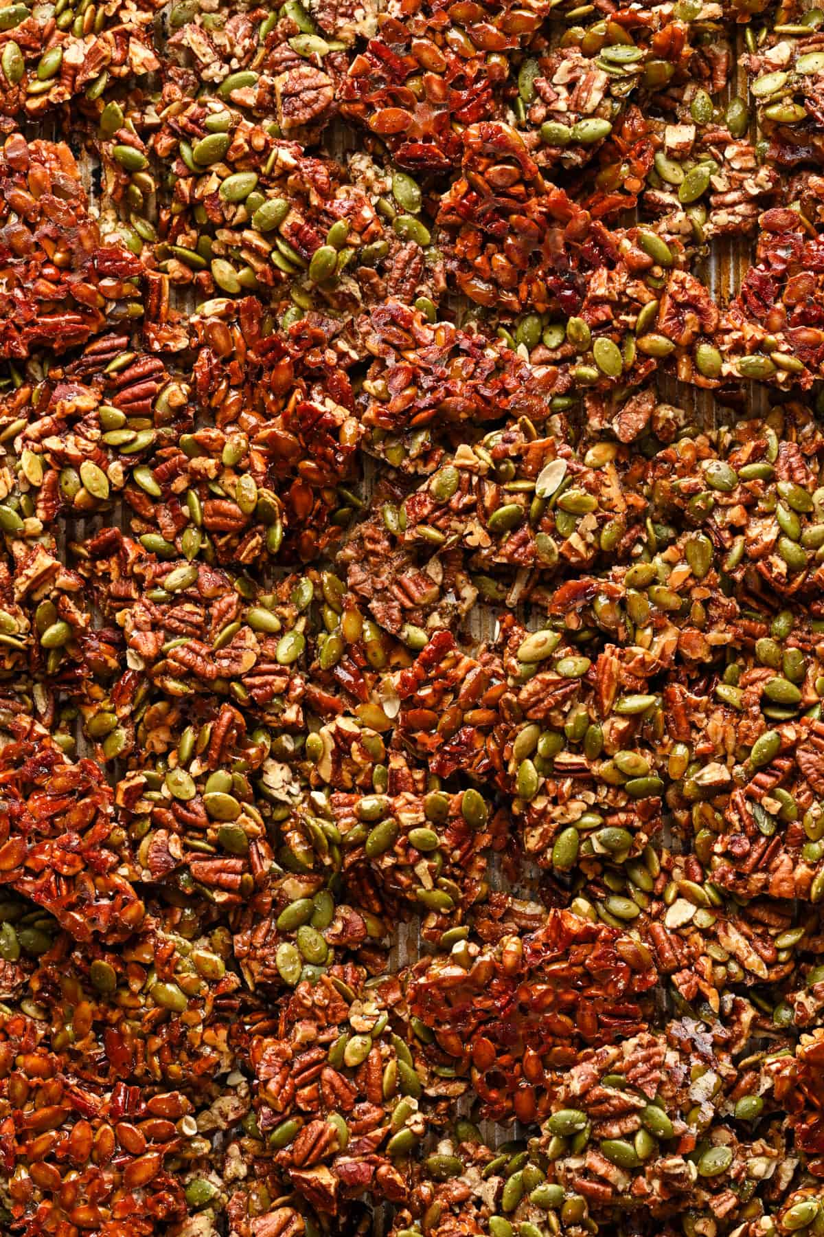 Pecan pepita brittle on baking sheet after baking, broken up into pieces.