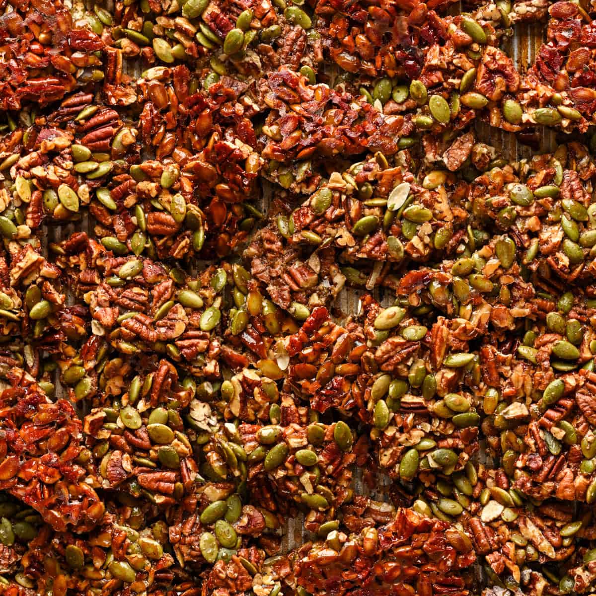 Pecan pepita brittle on baking sheet after baking, broken up into pieces.
