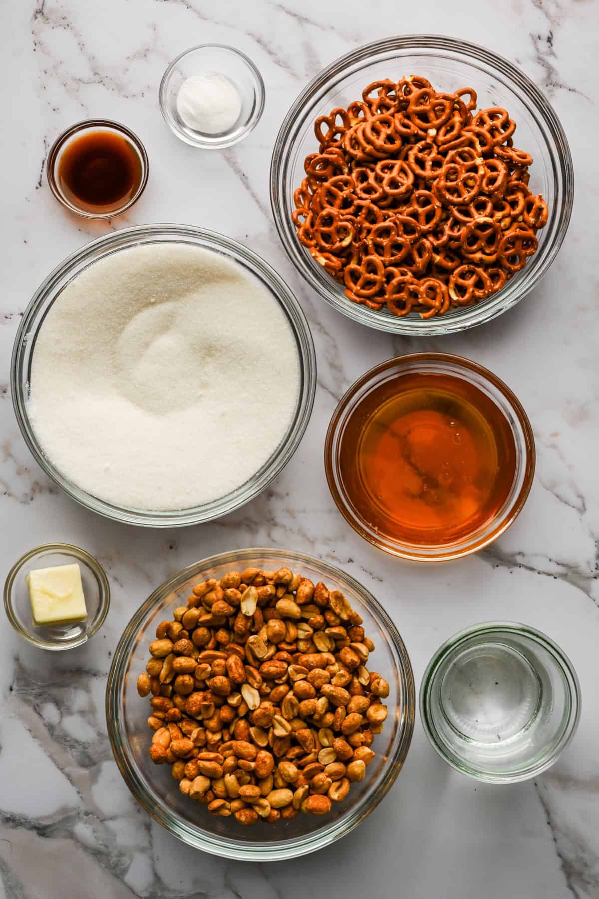 Overhead view of ingredients for pretzel peanut brittle on marble surface.