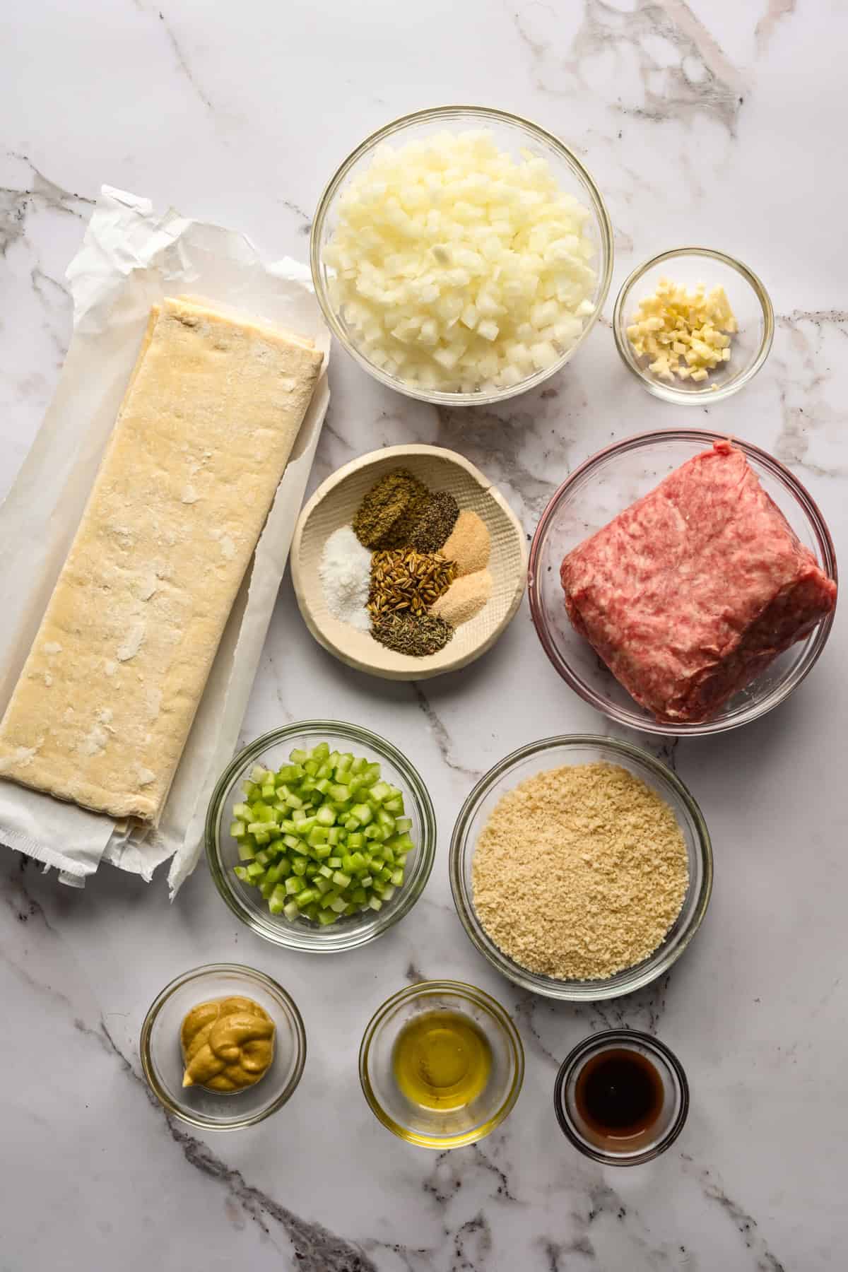 overhead view of ingredients for sausage roll wreath on marble surface.