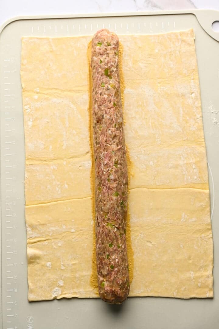 Large rectangle of puff pastry topped with long roll of sausage.
