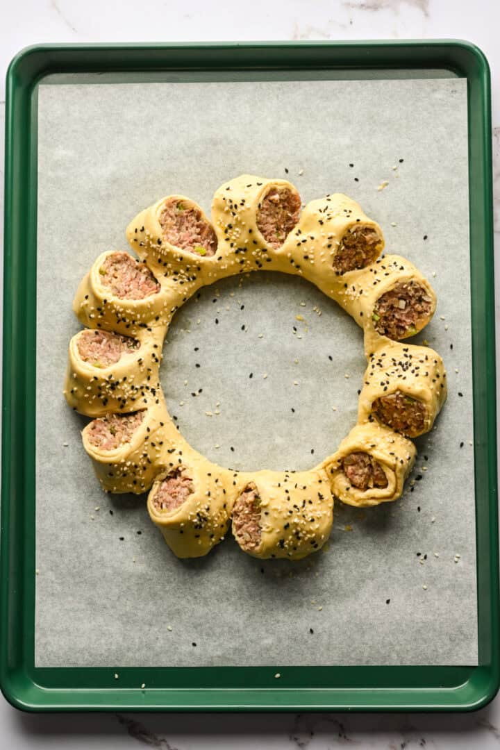 Sausage roll wreath on a baking sheet before baking.