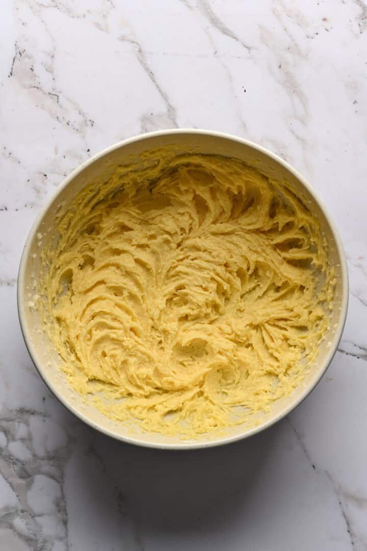 Butter, sugar and egg creamed in a white mixing bowl.