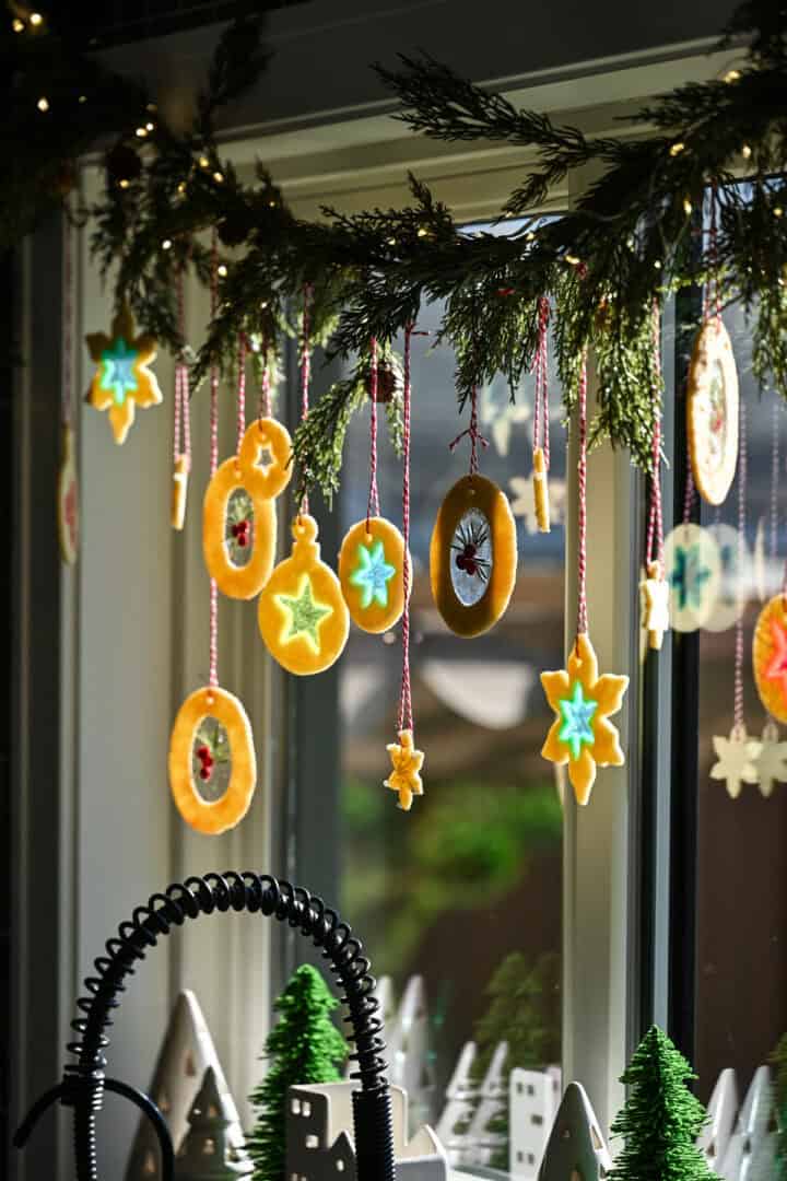 stained glass sugar cookies hanging from a garland in front of a kitchen window.