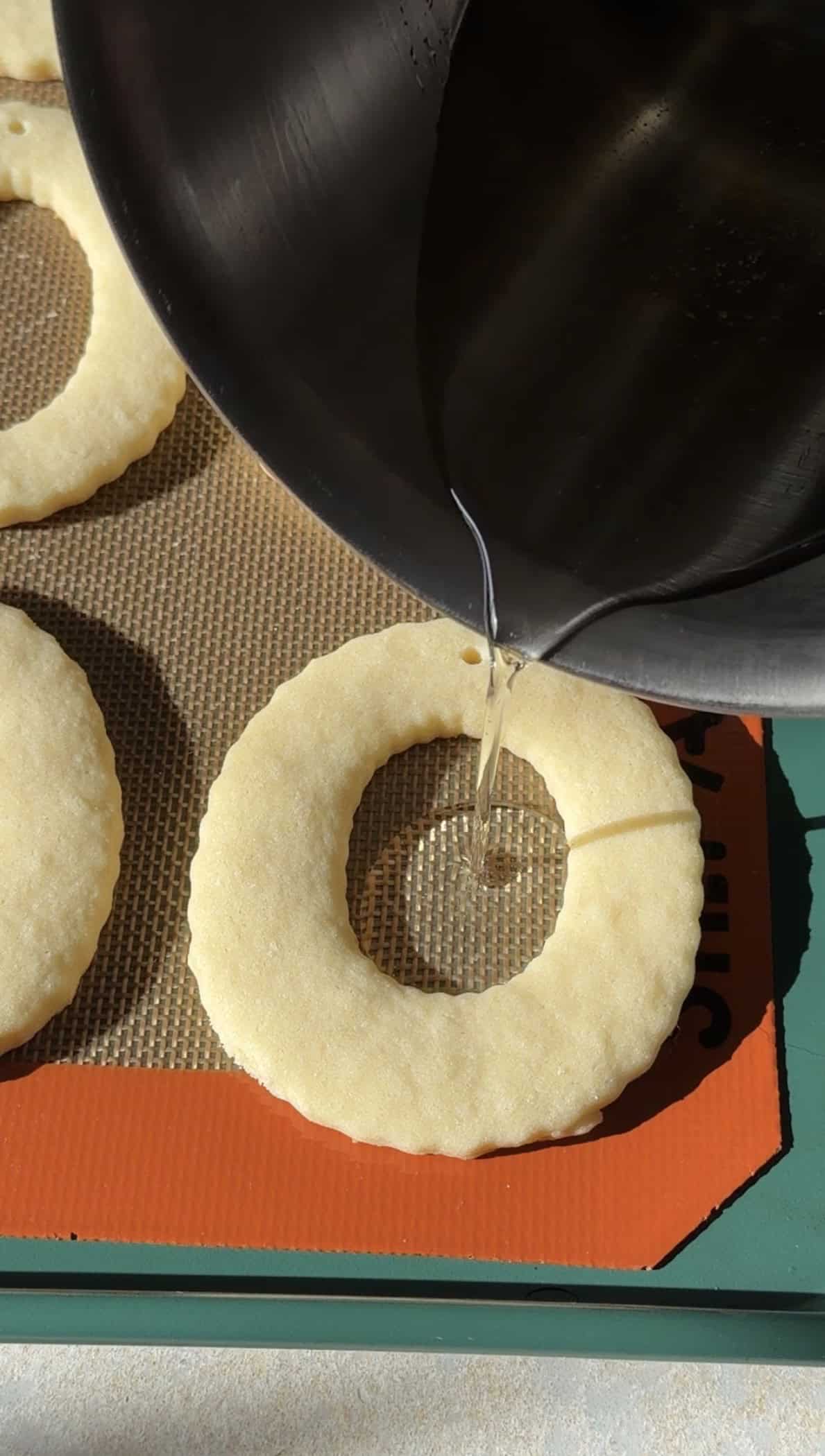 Pouring isomalt into an oval shaped sugar cookie with the center cut out.