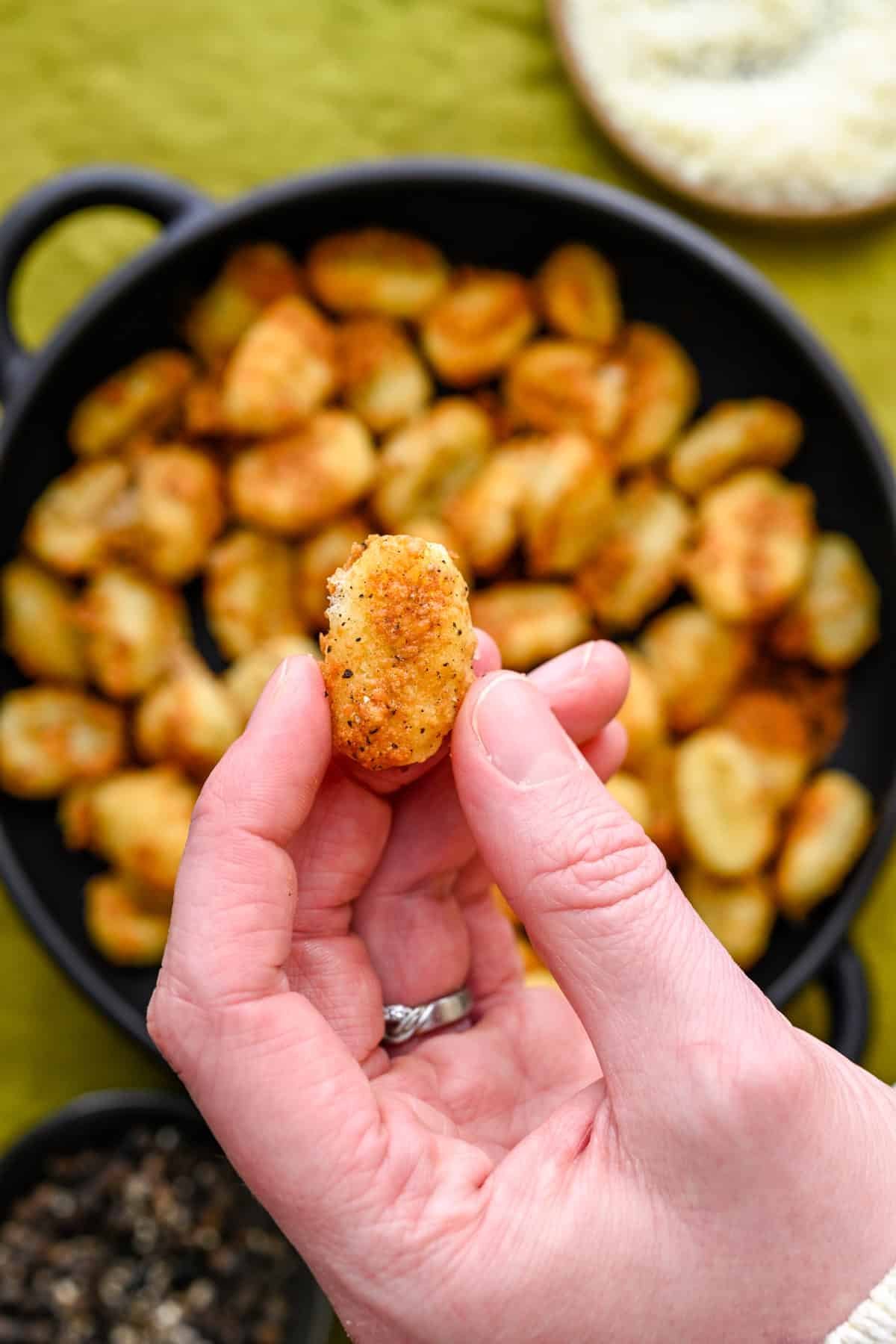 Hand holding up a single crispy cacio e pepe air fryer gnocchi.