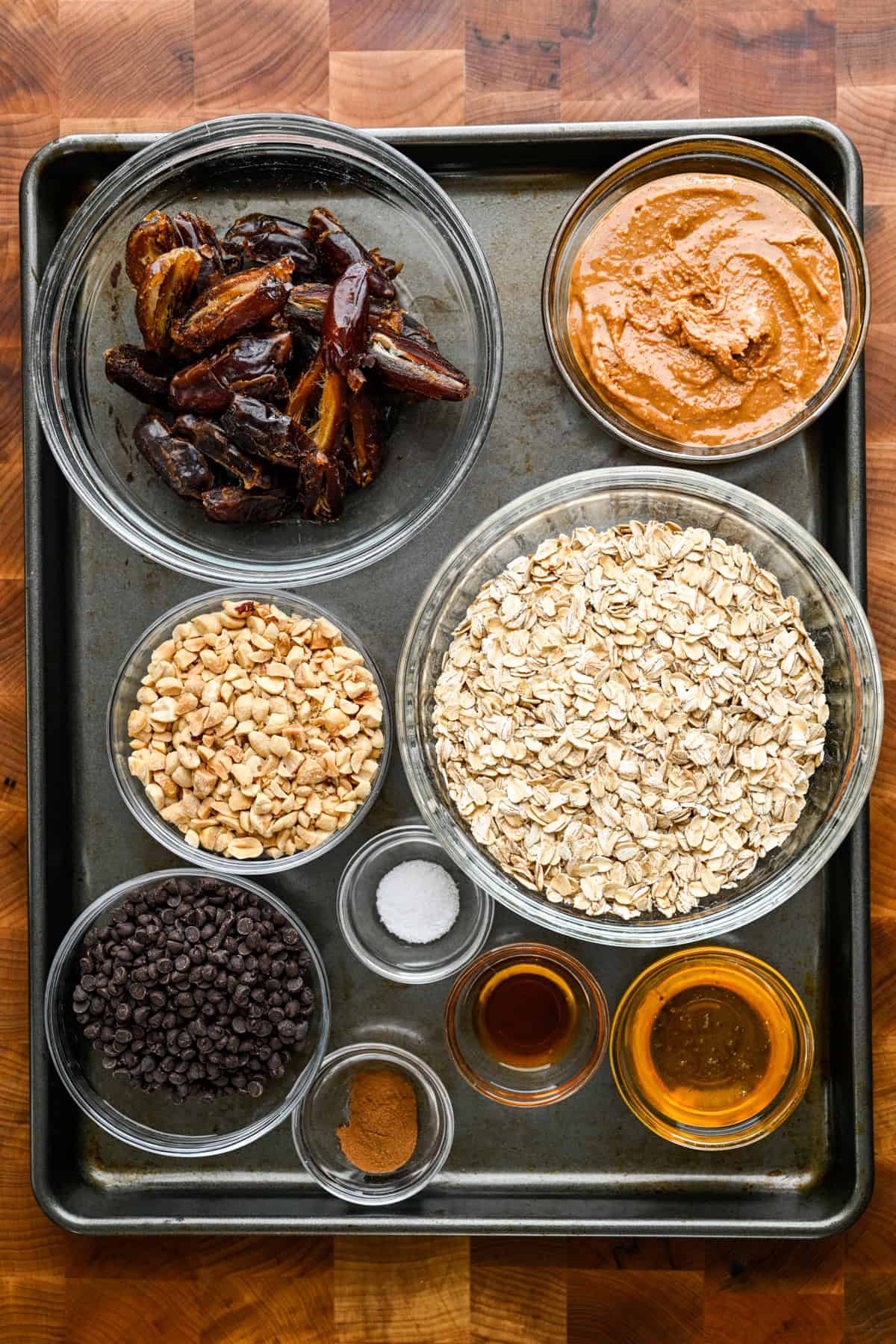 overhead view of ingredients for homemade peanut butter chocolate chip granola bars on a sheet pan in small bowls.