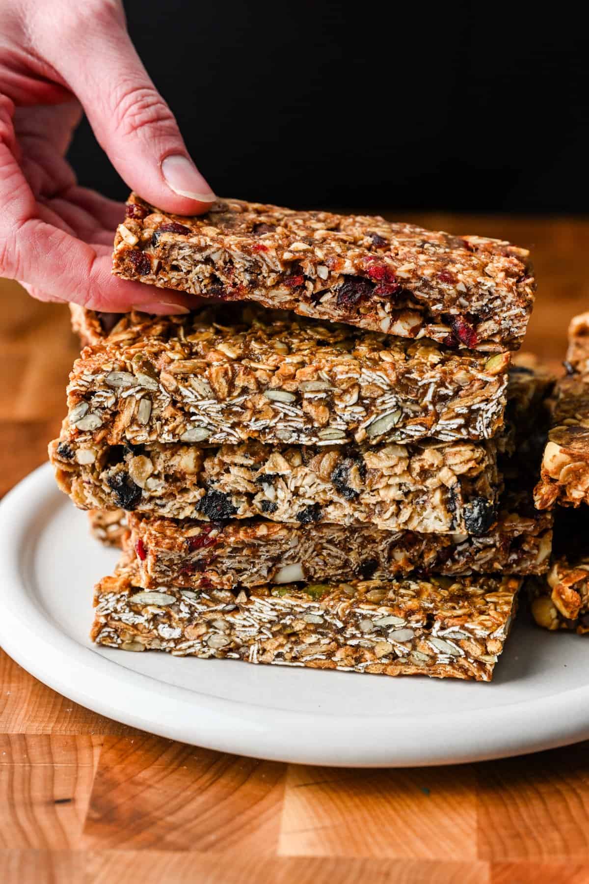 A stack of homemade granola bars with a hand reaching in to grab the one on top.