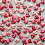 Overhead view of mini heart cookies with pink icing and heart sprinkles on parchment paper.