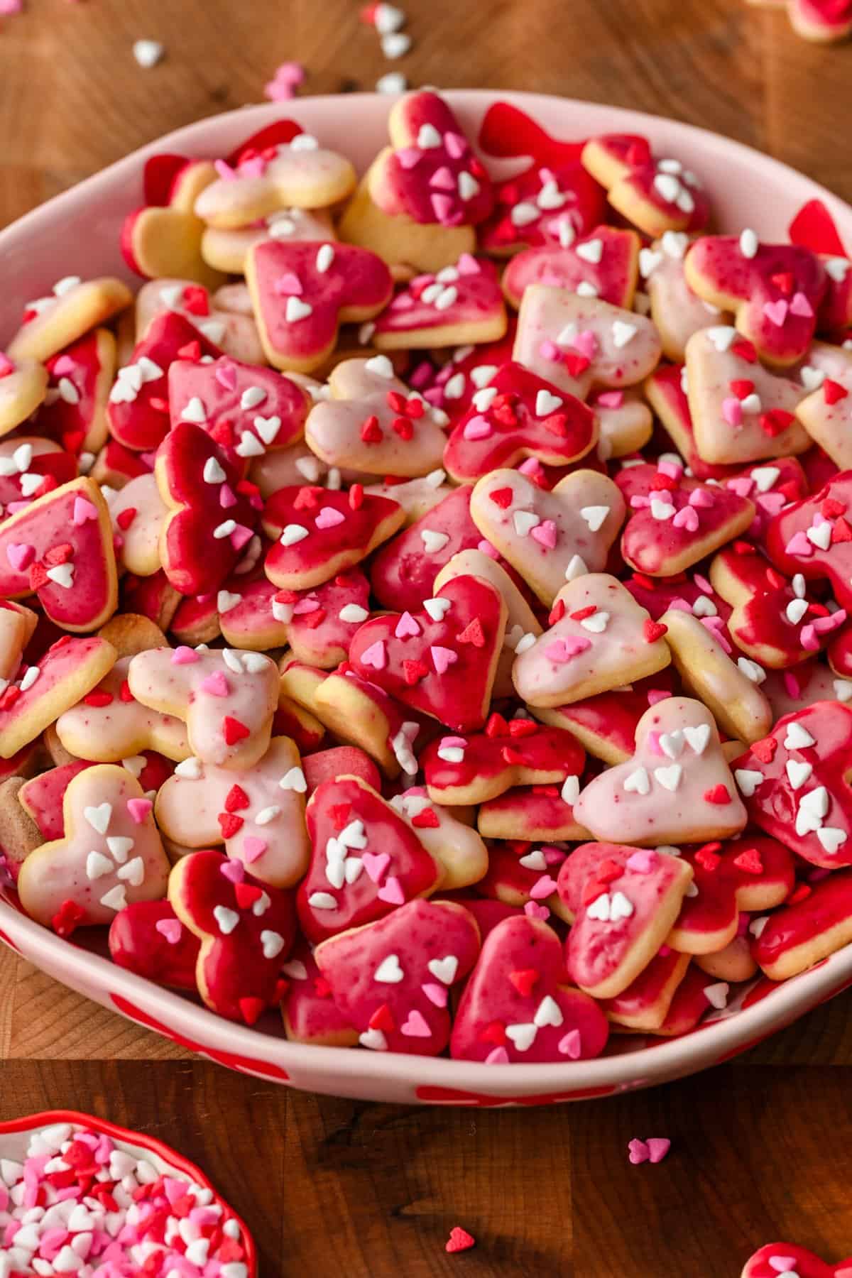 Close up view of mini heart cookies with pink icing and heart sprinkles in a pink bowl.
