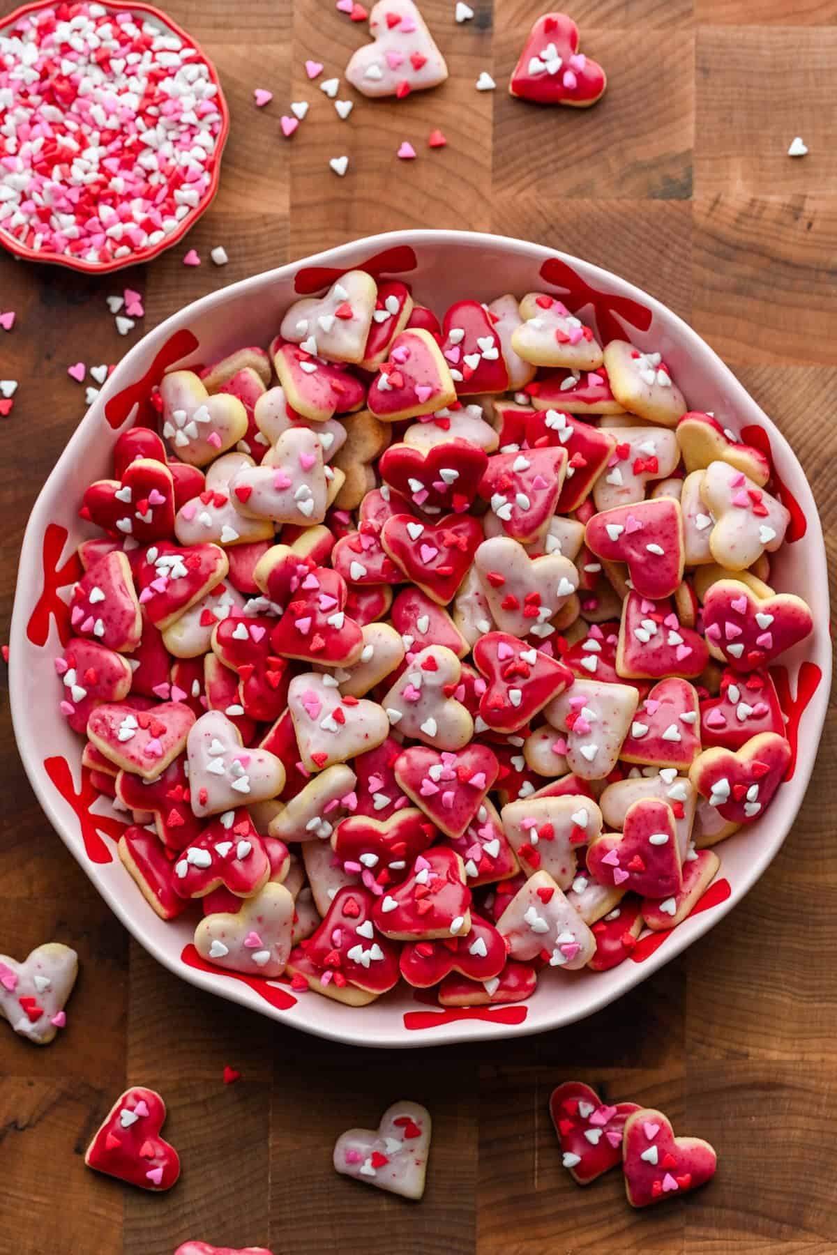 Overhead view of mini heart cookies with pink icing and heart sprinkles in a pink bowl.