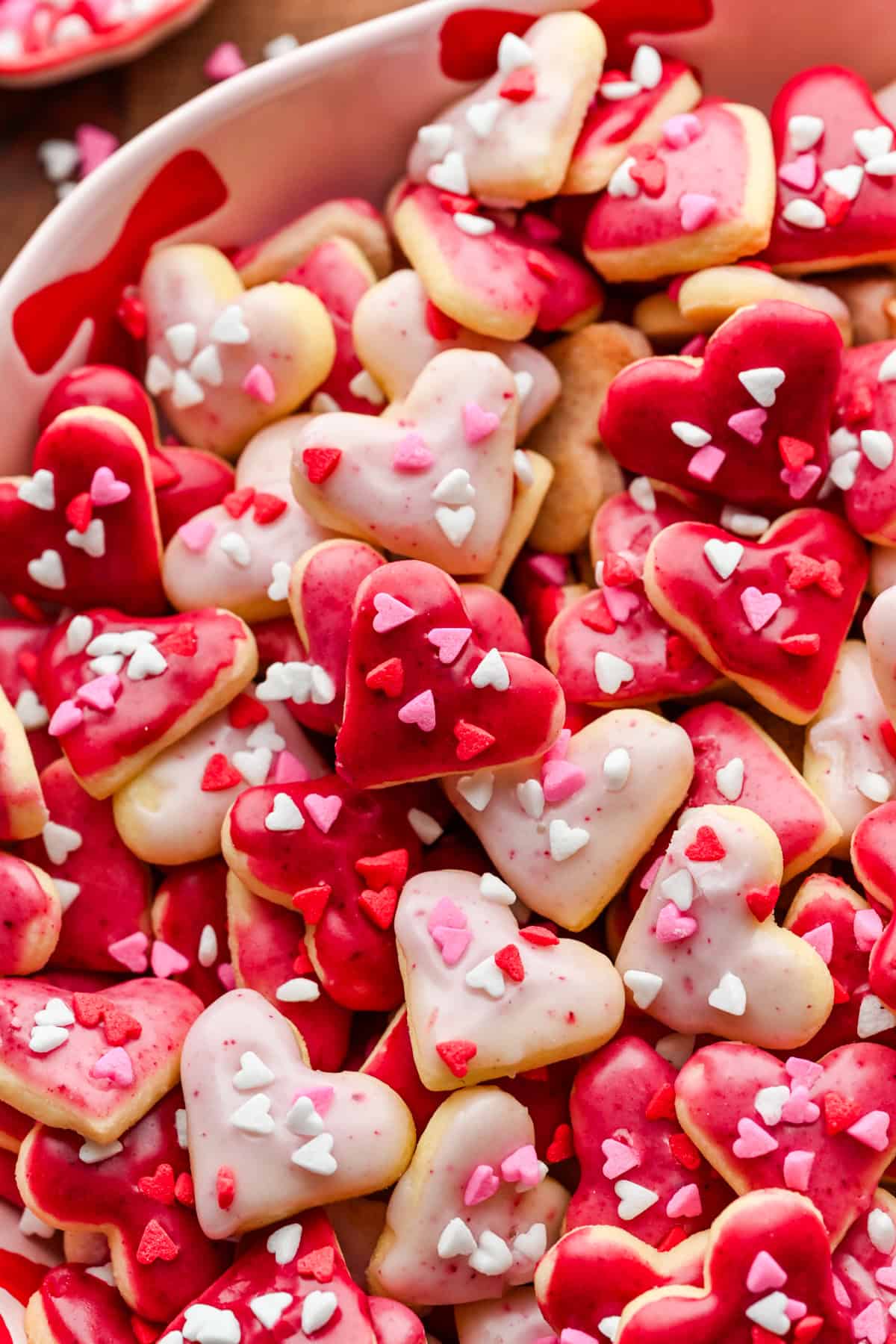 Close up view of mini heart cookies with pink icing and heart sprinkles in a pink bowl.