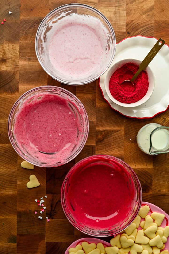 3 different shades of pink icing in glass bowls.
